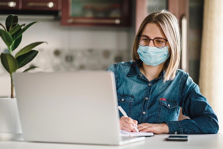 woman wearing a mask while using a laptop during the COVID-19 pandemic
