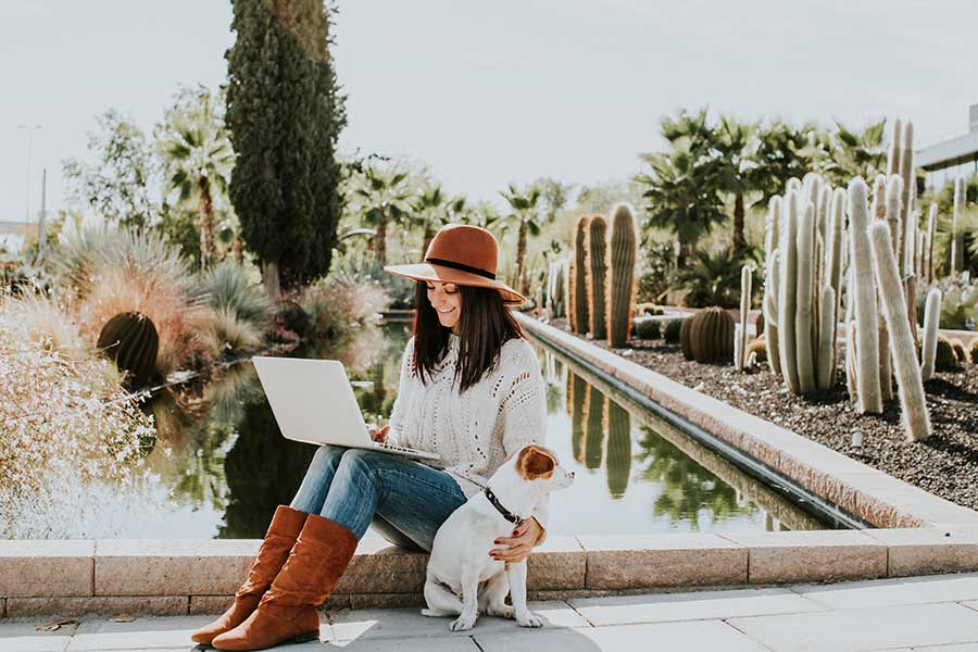 woman creating a budget for the new year on her laptop outside in a desert garden with her dog