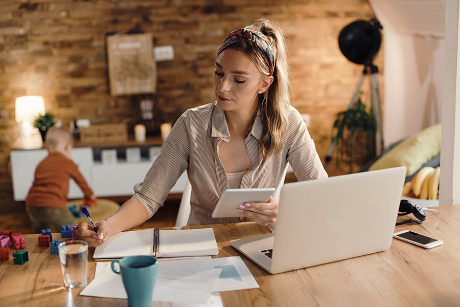 Hardworking mom planning her family's finances and creating a budget while her son plays with his toys.