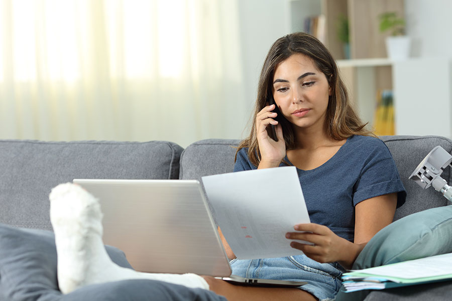 Young woman with her leg in a cast, on the phone paying her medical bills.