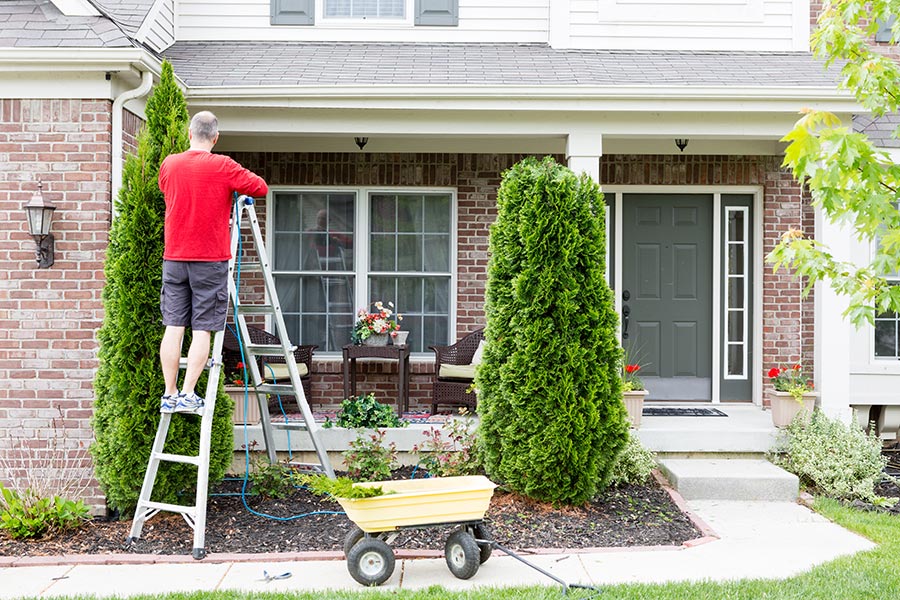 Man doing yard work on house. Home ownership checklist for first-time homebuyers.